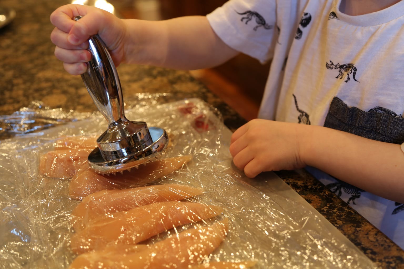 Child pounding chicken with meat mallet