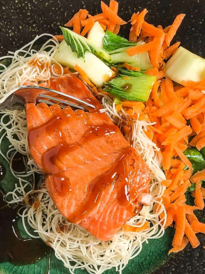 salmon and veggies on black plate drizzled with teriyaki sauce