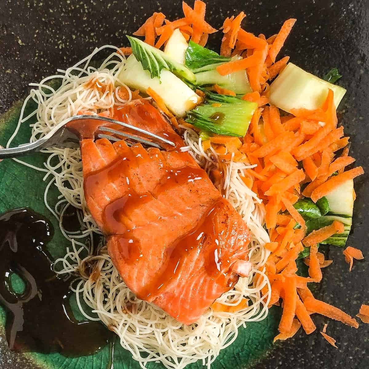 salmon and veggies on black plate drizzled with teriyaki sauce