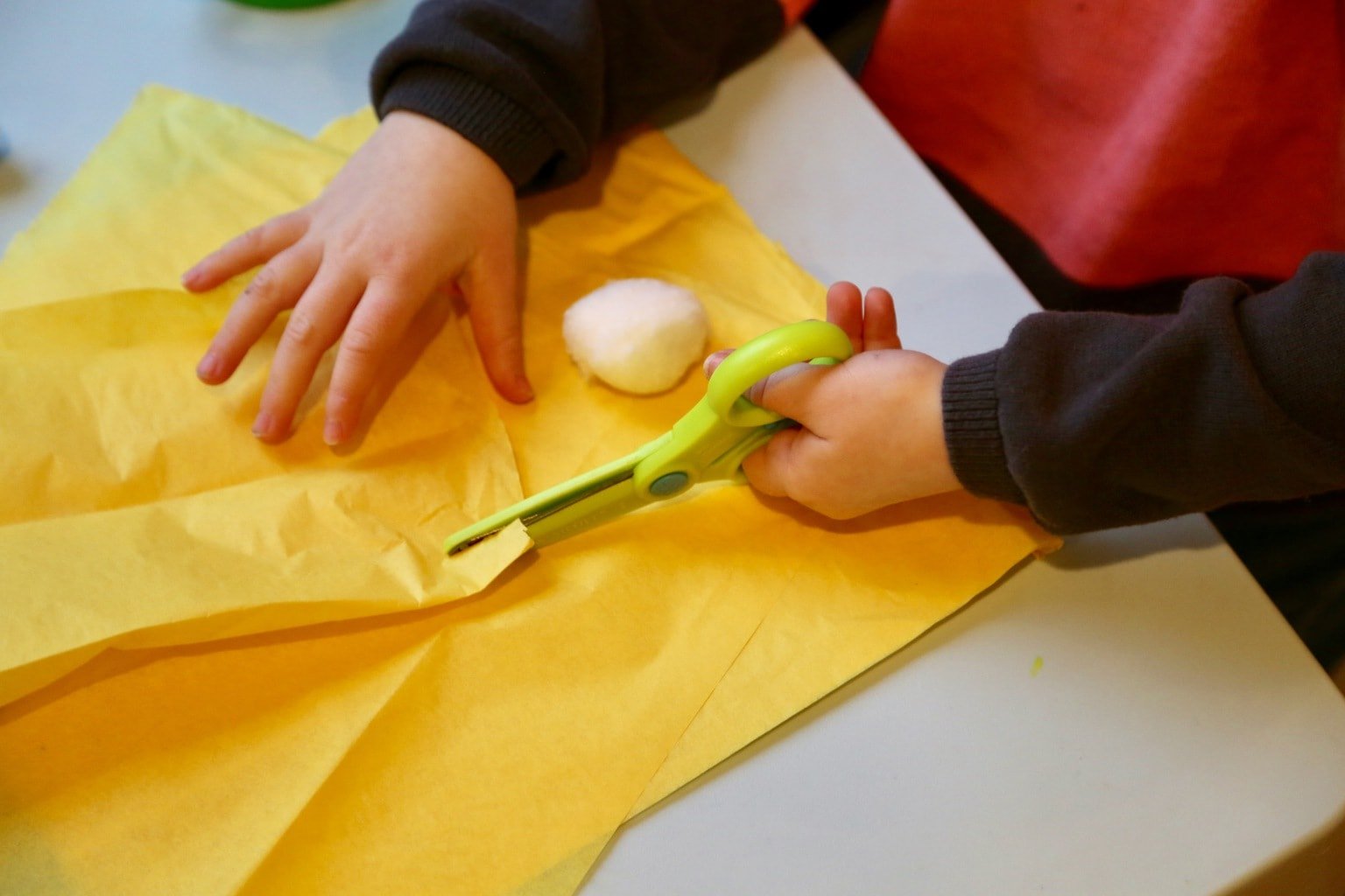 Child cutting yellow tissue paper for play food tortellini