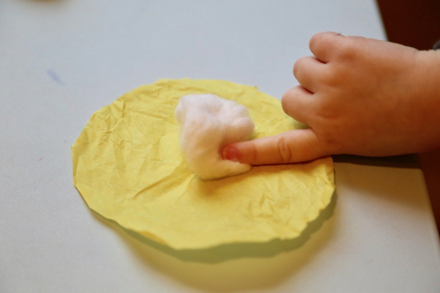 Child placing cotton ball on yellow circle
