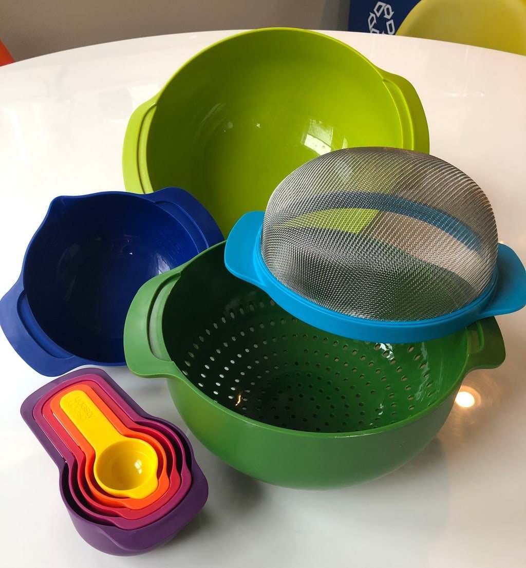 set of colorful nesting bowls, measuring cups and strainers spread out on white table