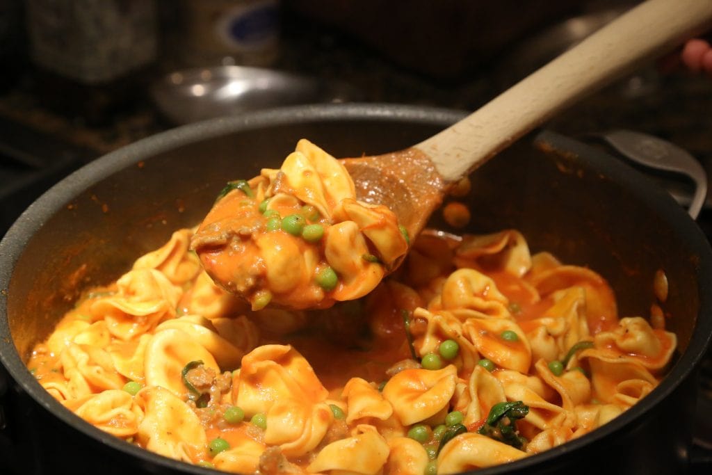 Wooden spoon scooping up cheese tortellini sauce with peas