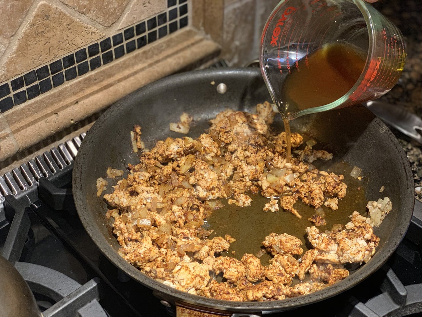 Child adding cup of beef broth to pan