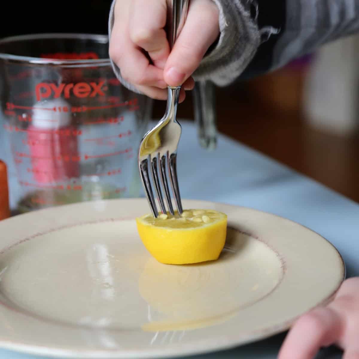 Fork stabbing holes into a halved lemon. 