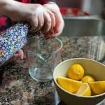 mom and child hands squeezing lemons into pyrex measuring cup