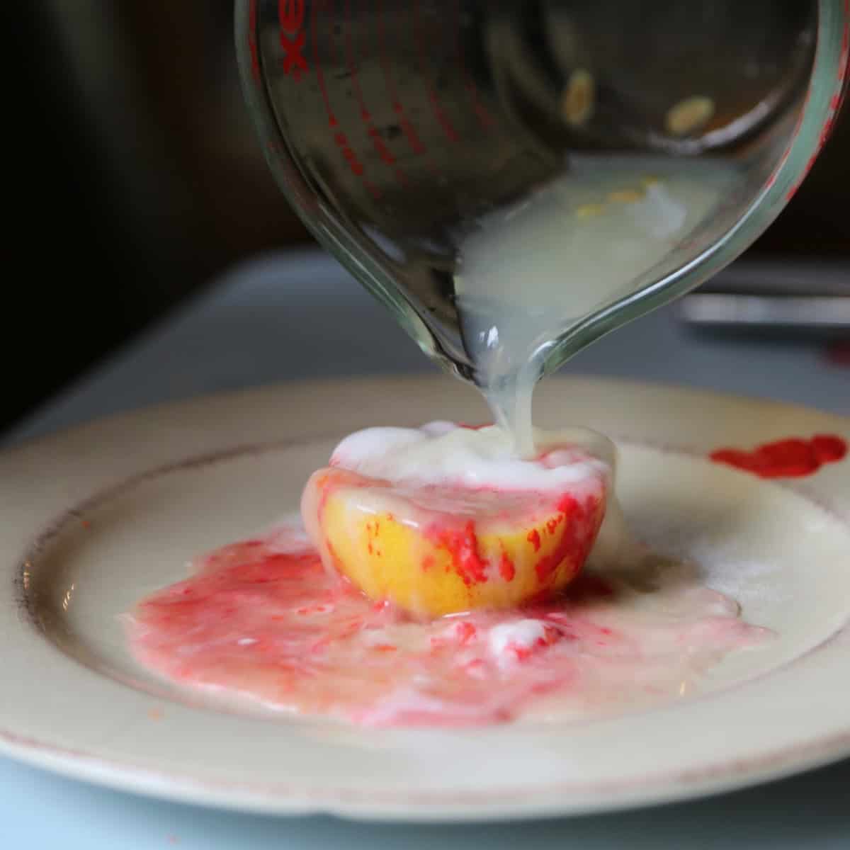 Pouring lemon juice onto halved lemon with baking soda and red paint to form a lemon volcano eruption. 