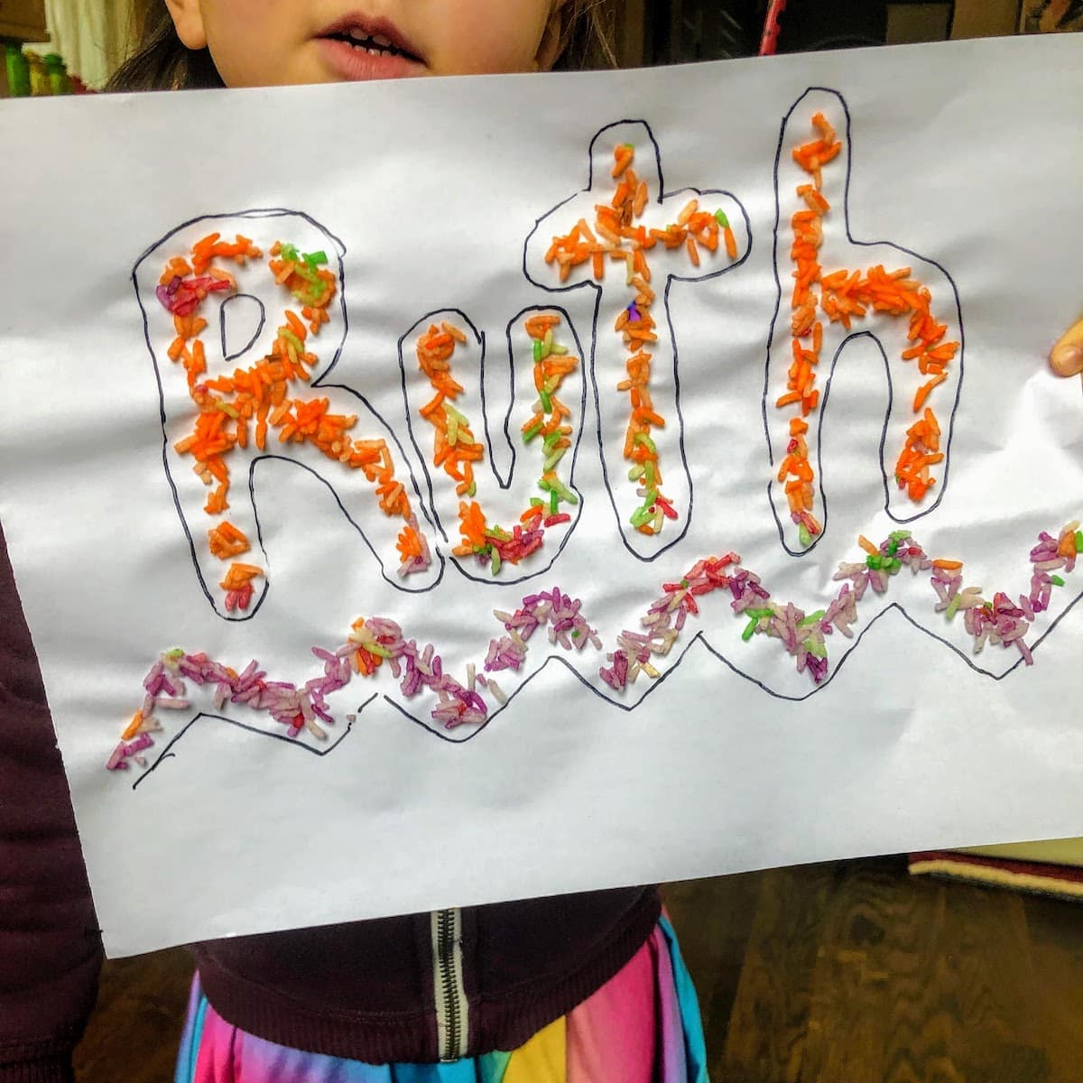 child holding paper with name written in colorful rice letters