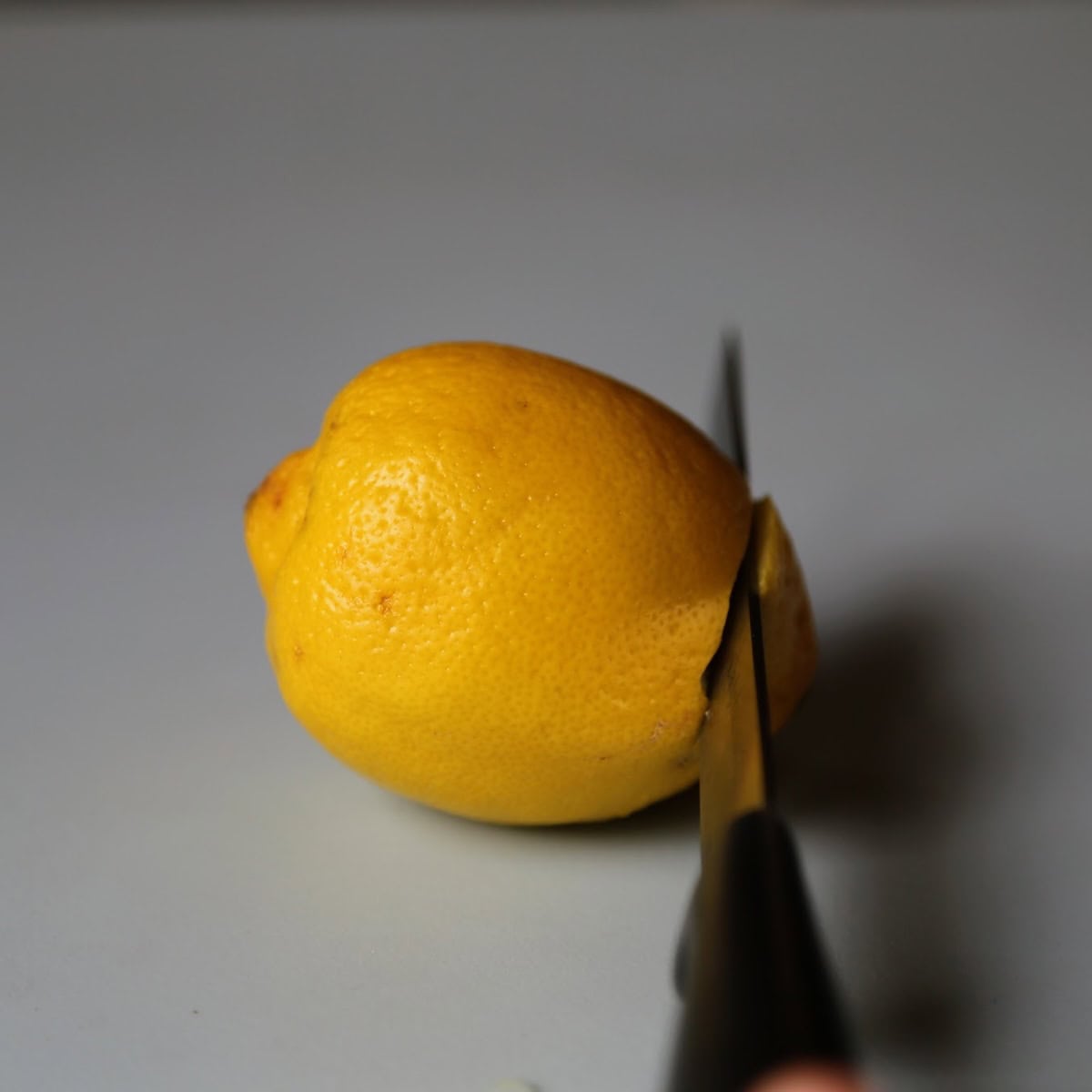 Knife slicing tip off of whole lemon. 