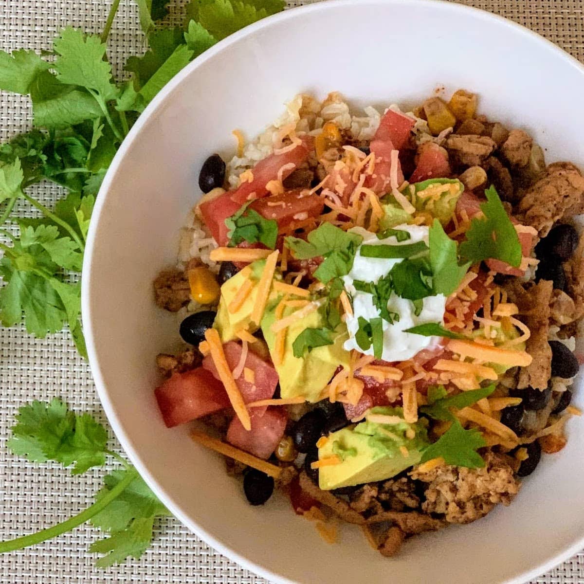 white bowl with ground turkey, taco toppings and cilantro