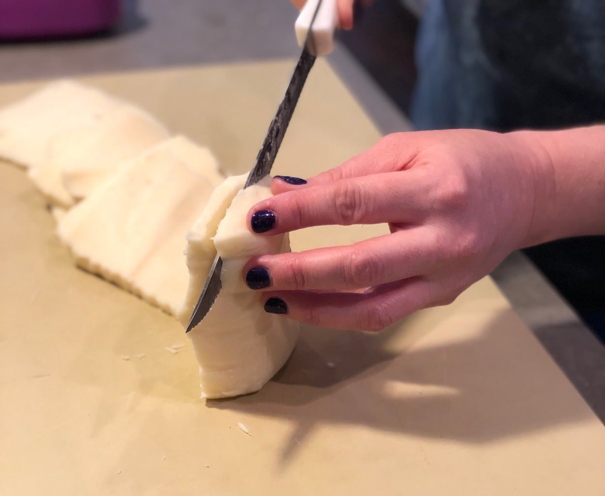 hand with black nail polish slicing mozzarella cheese on manila cutting board