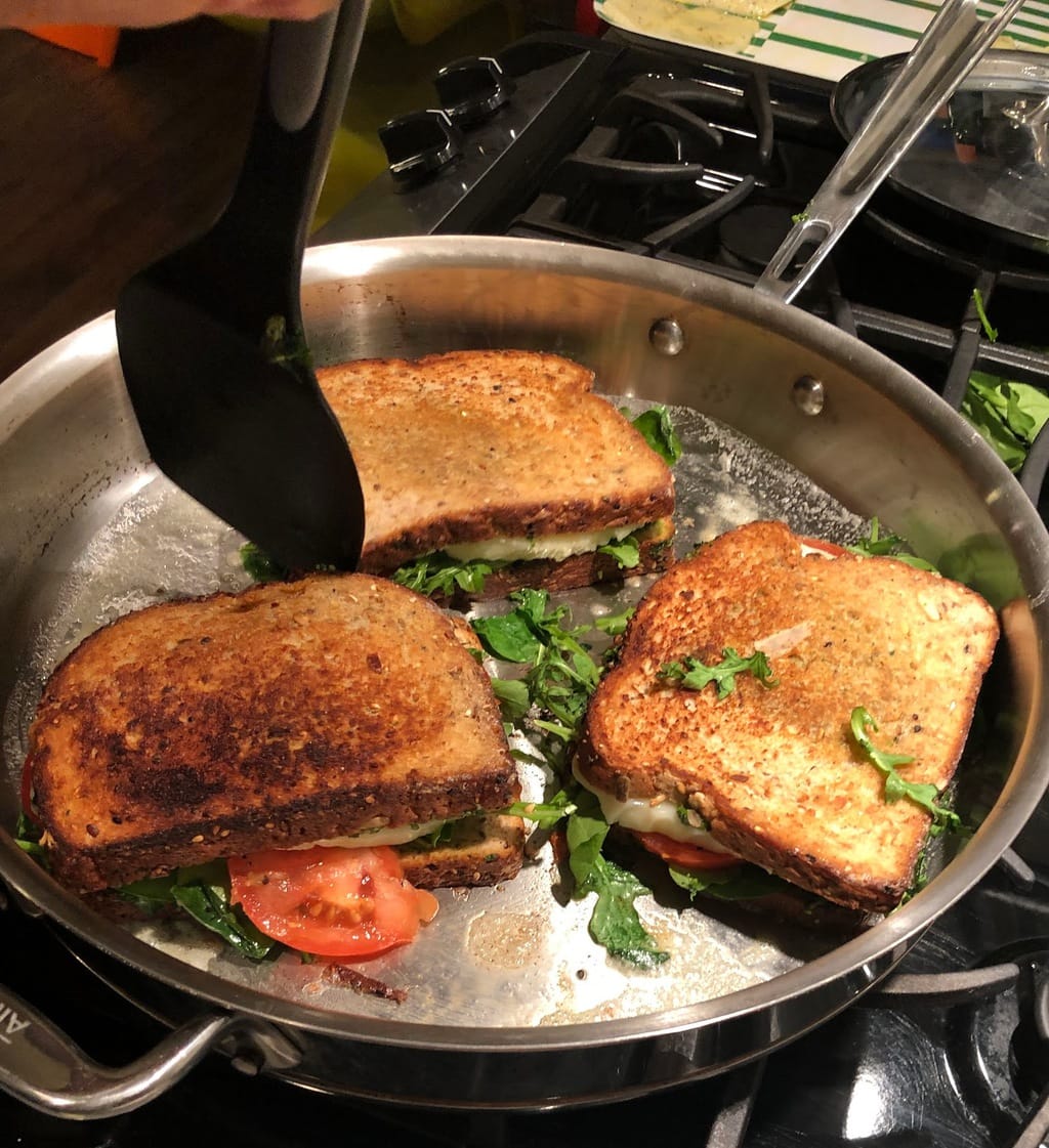 three pesto paninis toasting in pan with spatula about to flip one over