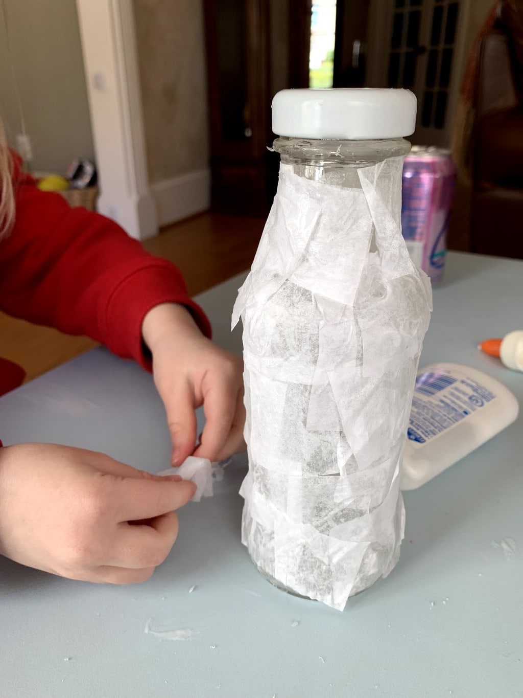 Child gluing white tissue paper on bottle