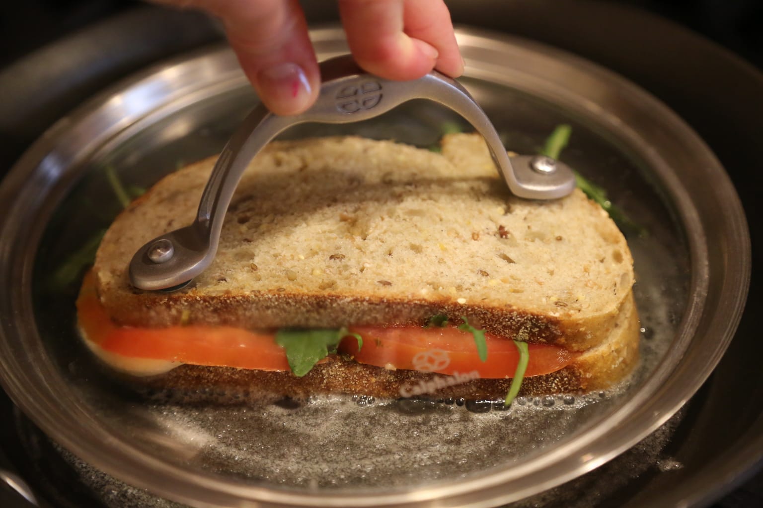 Child pressing down panini with a pan's lid as it cooks on stove