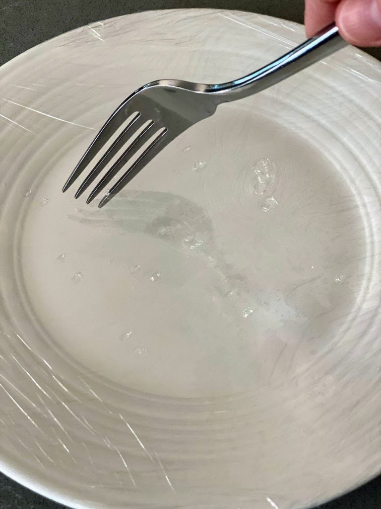 white plate wrapped in plastic wrap with fork poking holes in top