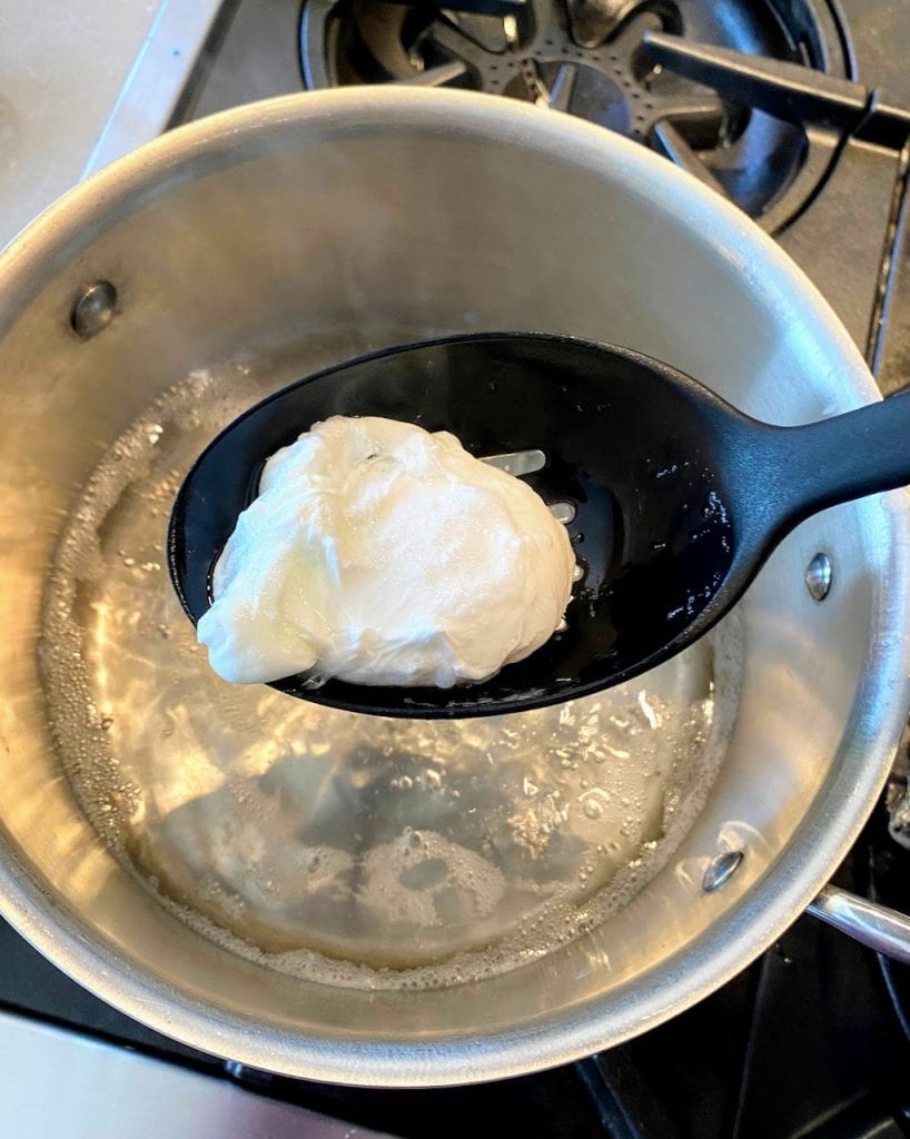 slotted spoon getting poached egg out of pot