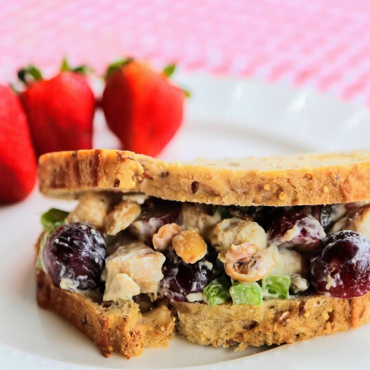 chicken salad sandwich on gingham blanket with strawberries