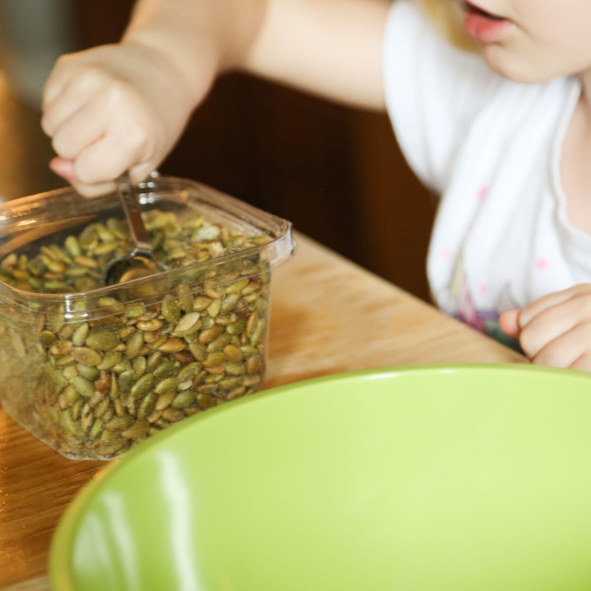 kid scooping pumpkin seeds to go into big green bowl