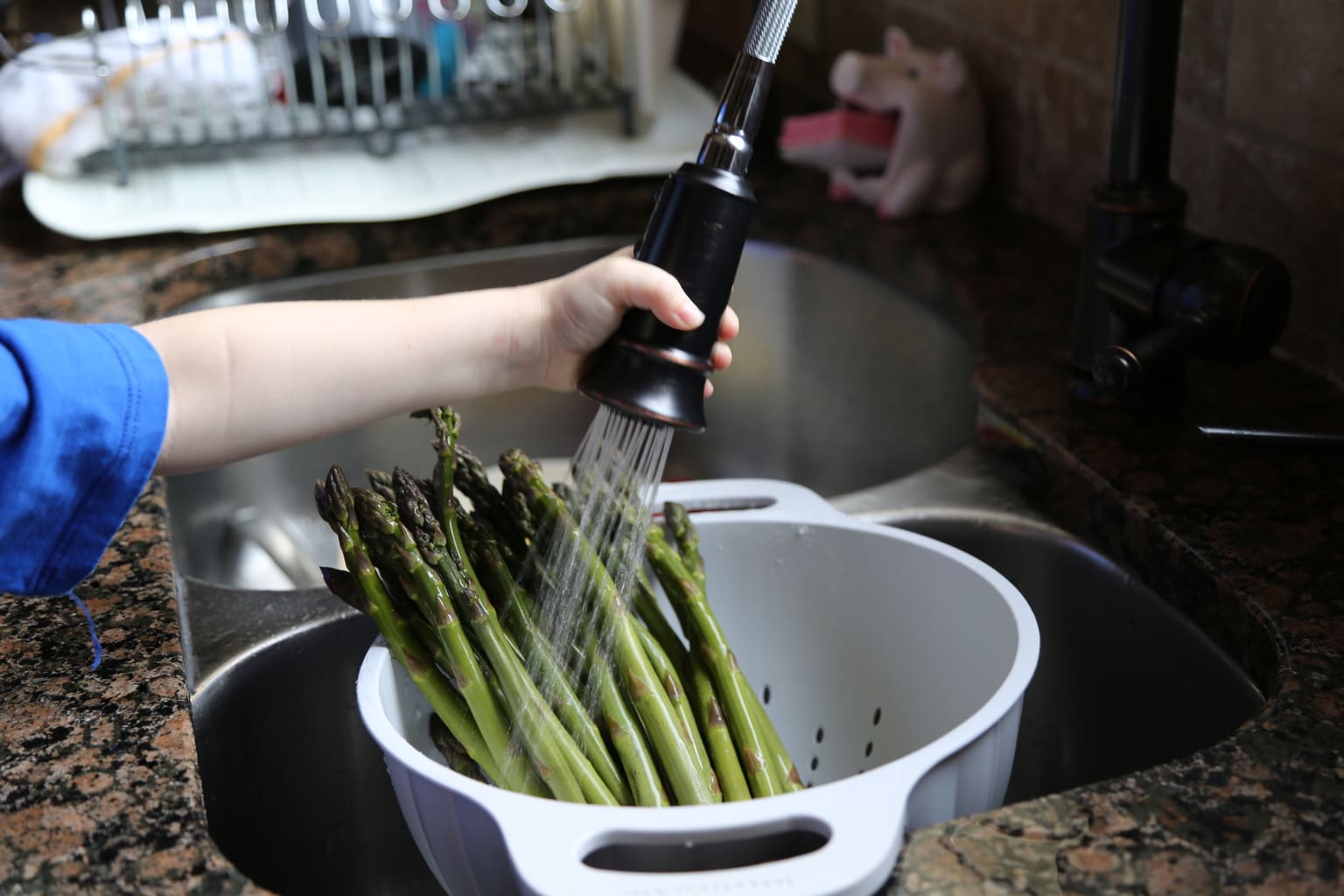 child washing asparagus in strainer