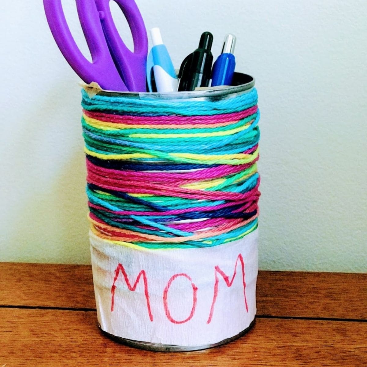 empty tin can decorated with yarn and filled with writing utensils