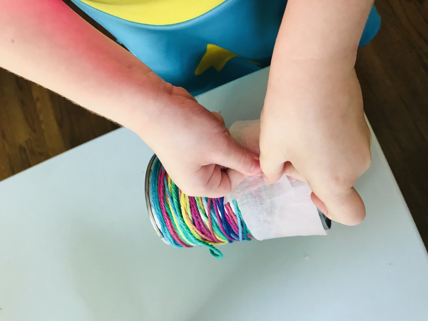 child taping tissue paper onto can