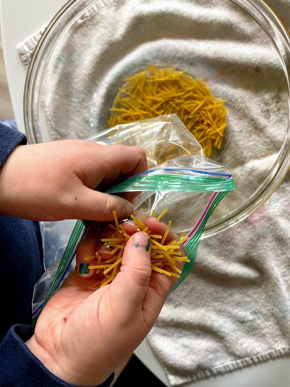 child and parents putting broken spaghetti noodles into ziploc bag