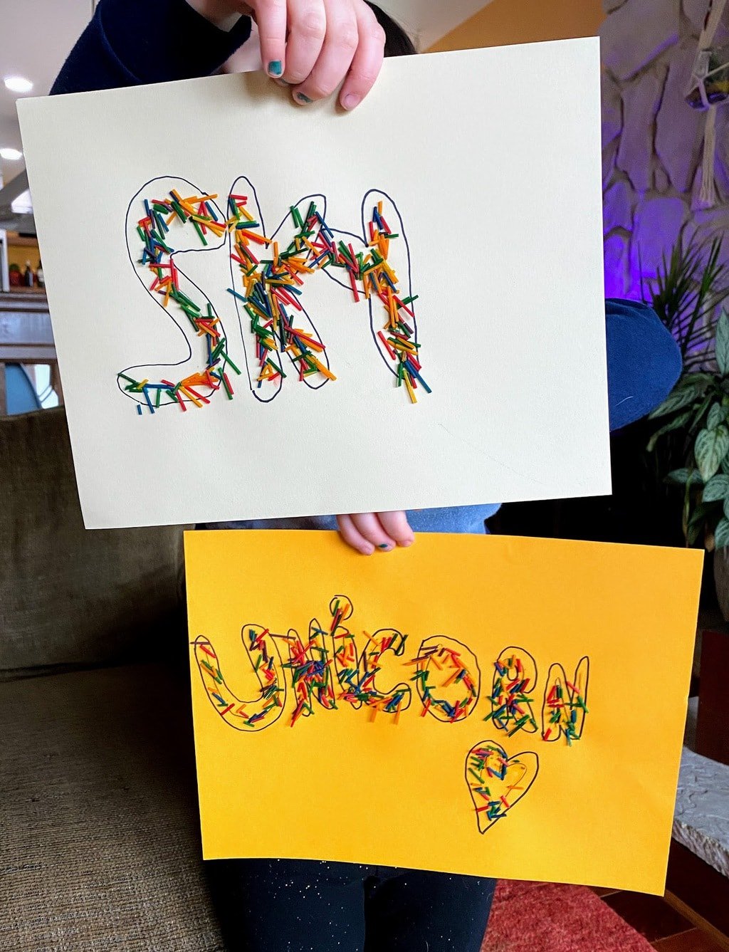 child holding rainbow spaghetti art with words sky and unicorn