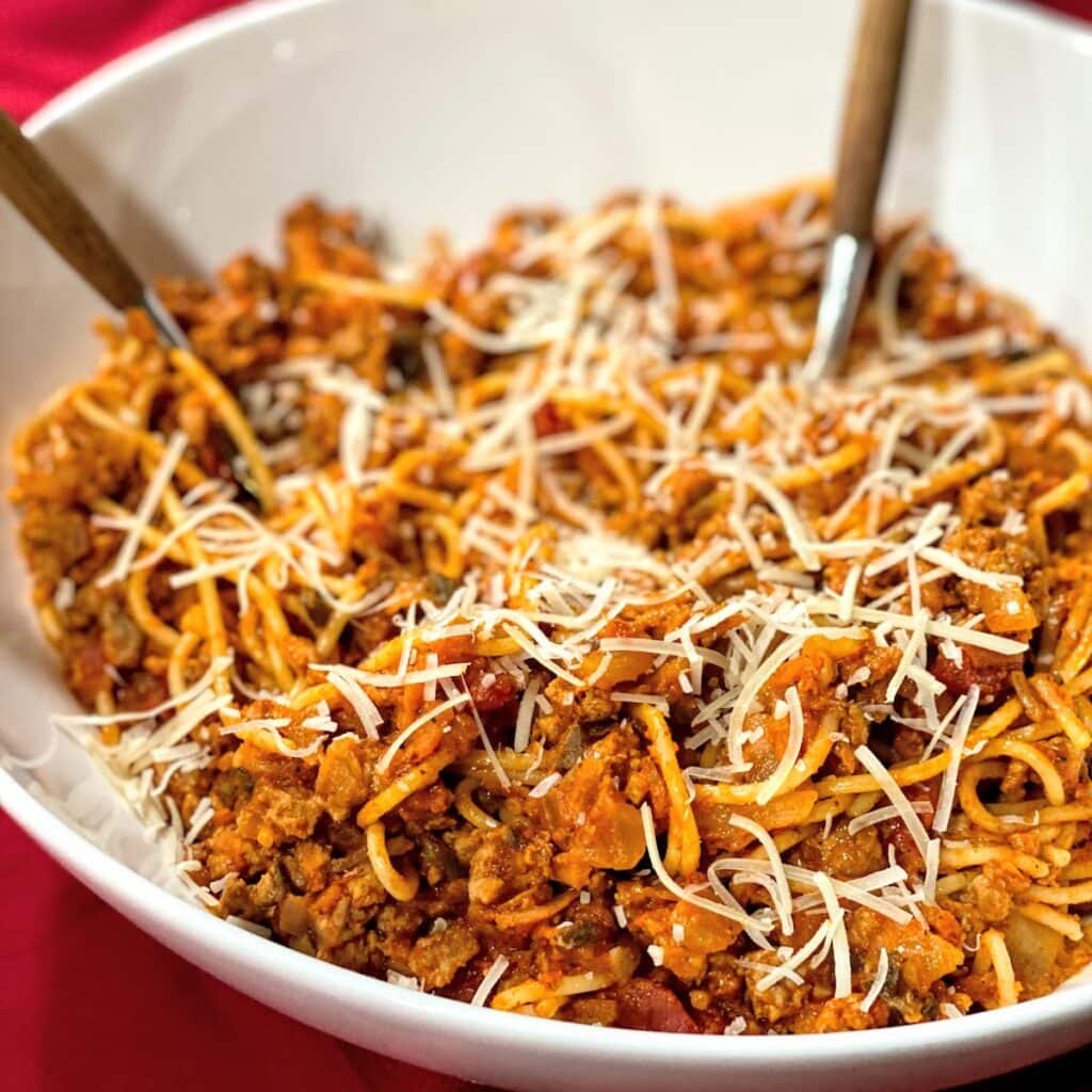 white, big bowl of spaghetti with meat sauce and cheese on red tablecloth