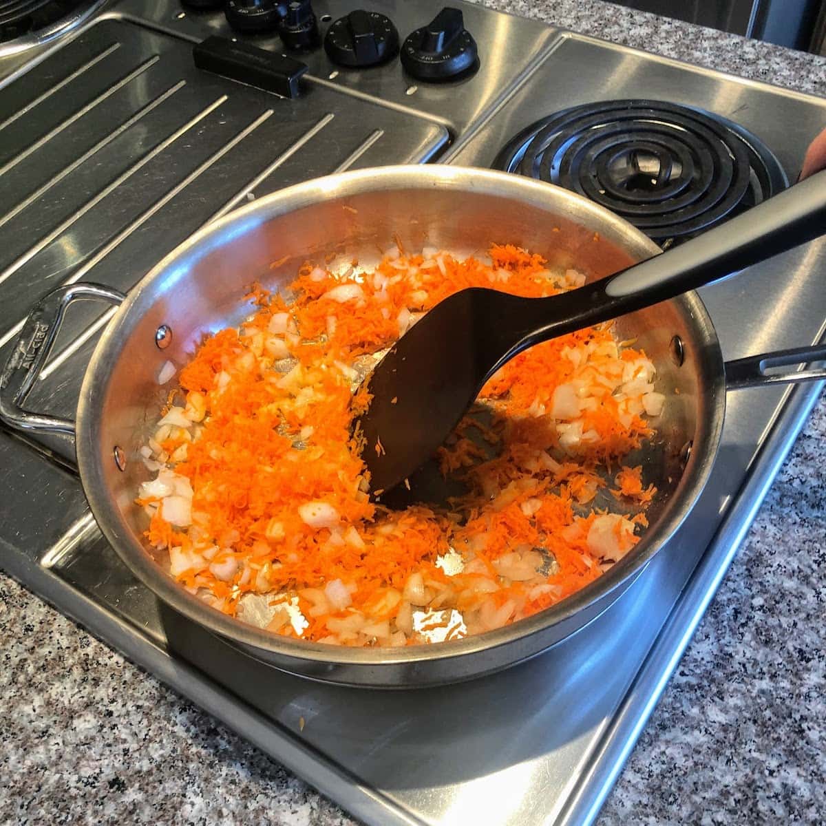 stirring pan of carrots and onion on stovetop