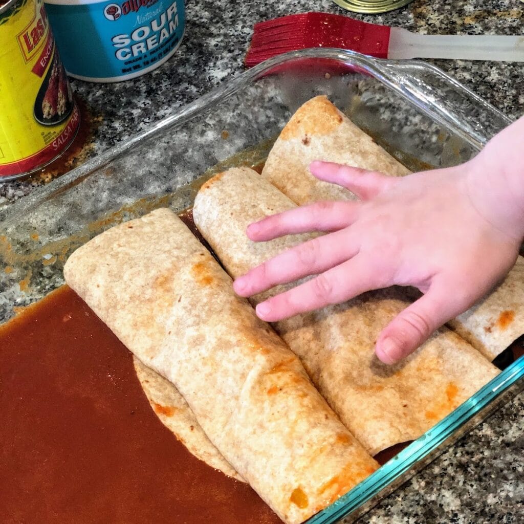 child placing enchiladas in dish