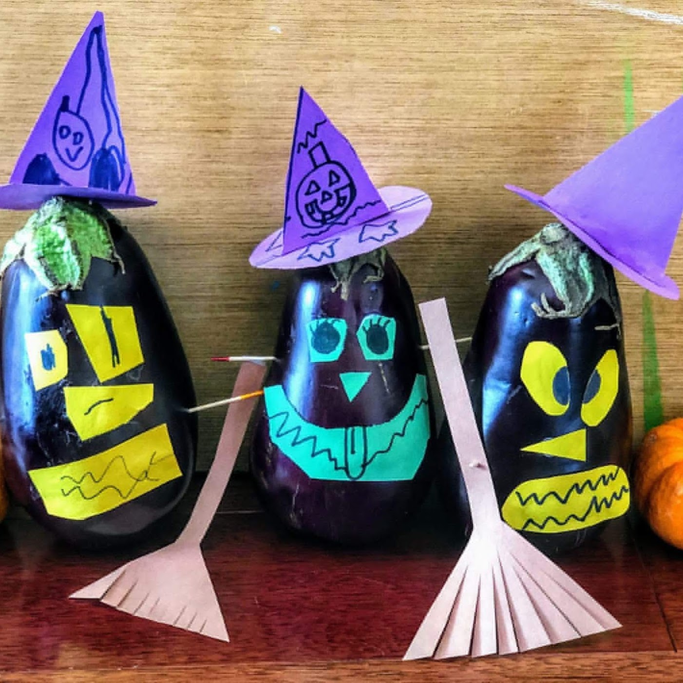 three eggplants decorated as witches with paper: purple hats, bronw booms, and green/yellow spooky faces