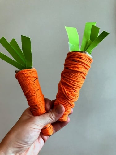 hand holding two play food carrots
