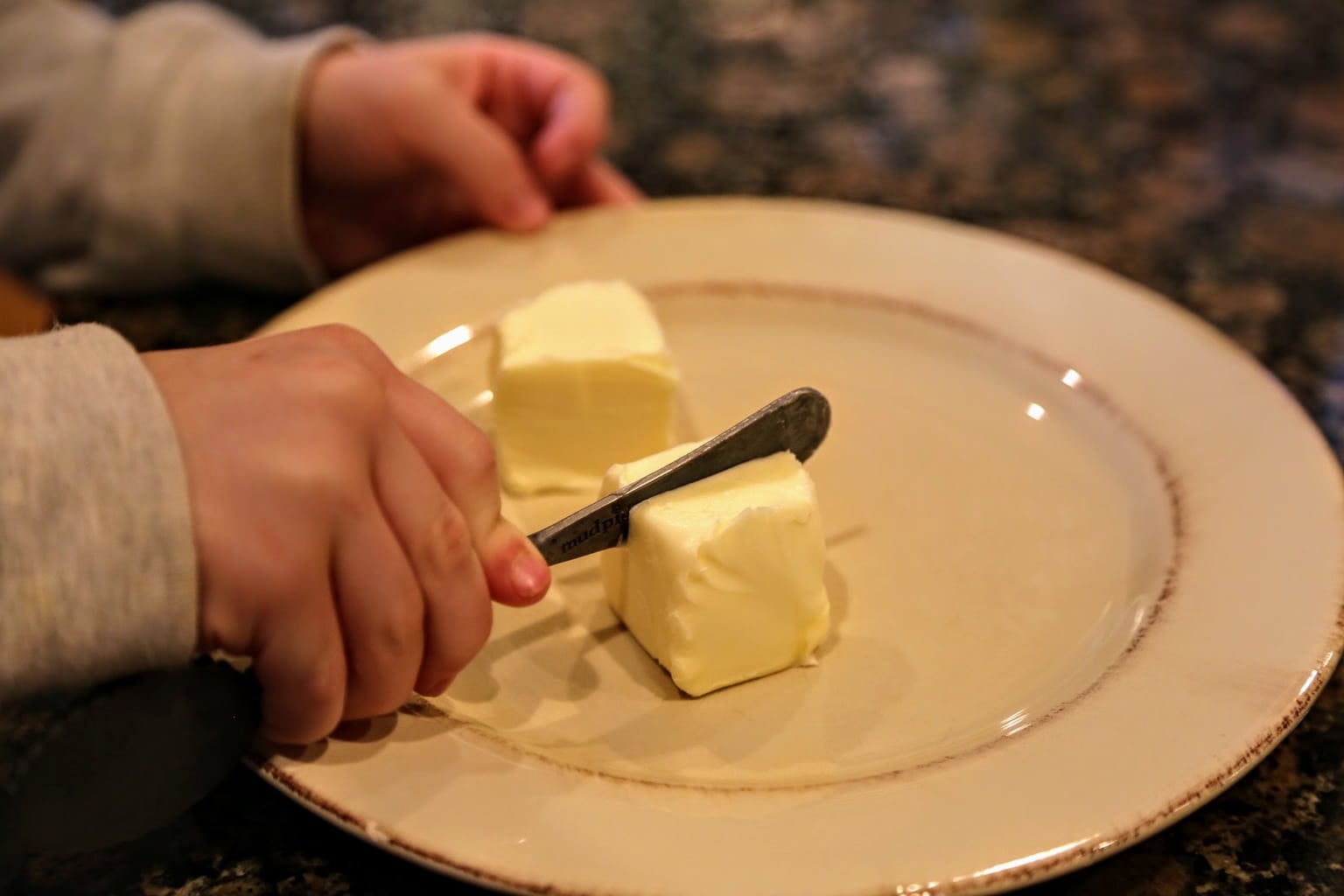 child cutting butter on plate