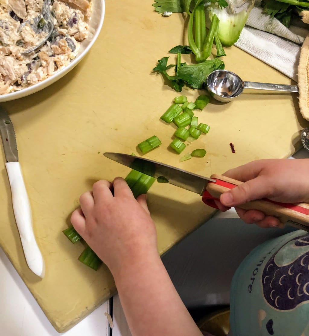 Child cutting celery on manila cutting board, for chicken salad