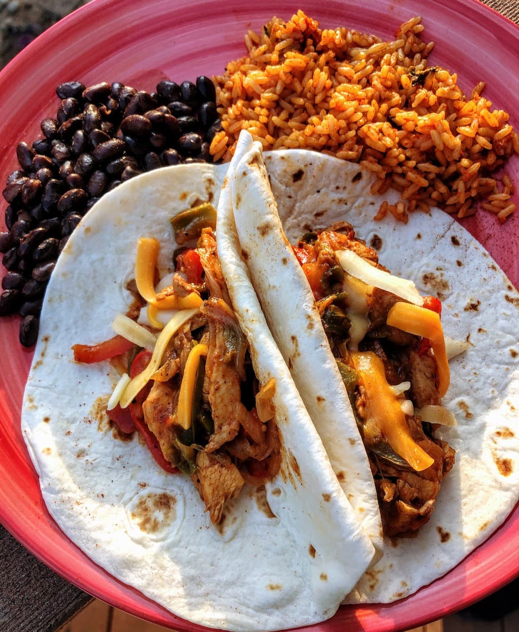 chicken fajitas with cheese, rice and beans on a pink plate