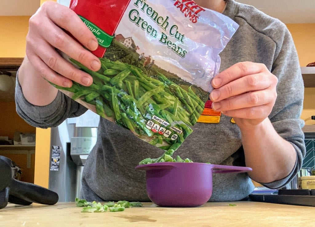 pouring frozen green beans from bag into purple measuring cup