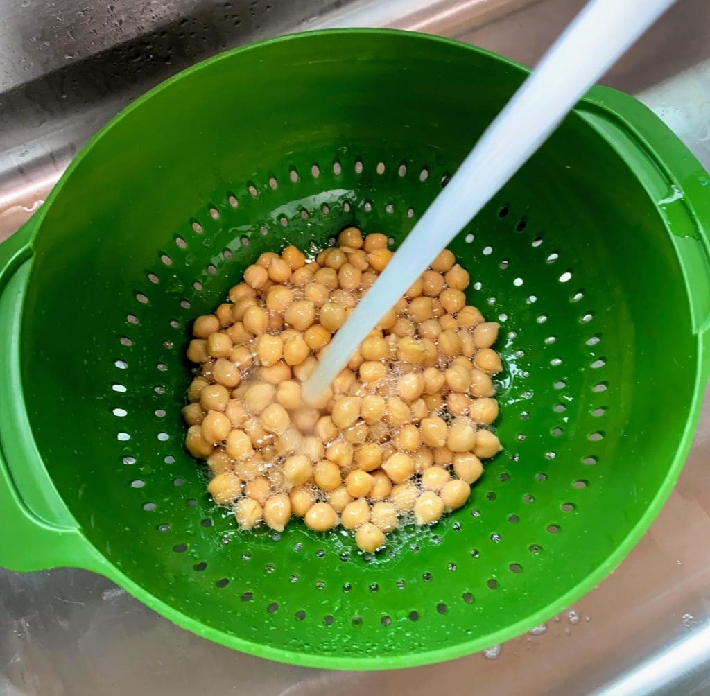 rinsing chickpeas in green colander in sink