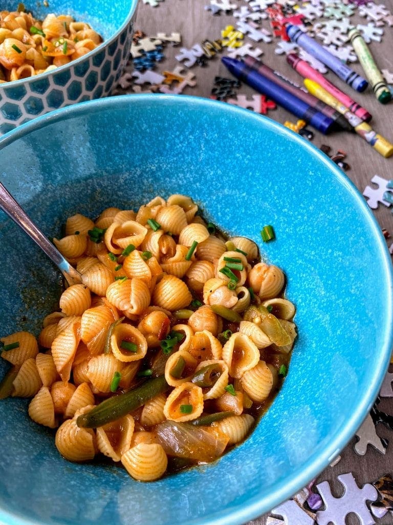 pasta with chickpeas and chives in blue bowl on table with puzzle pieces and crayons