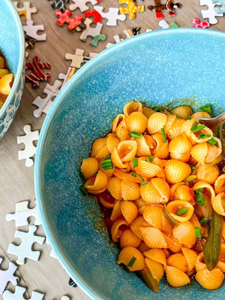 pasta with chickpeas and chives in blue bowl on table with puzzle pieces
