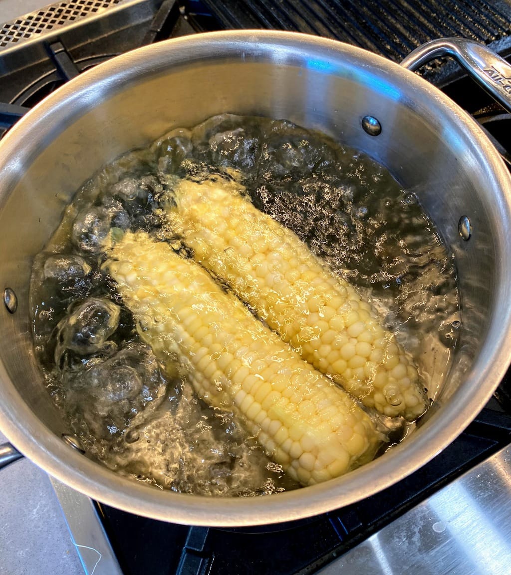large pot filled with boiling water and 2 ears of corn