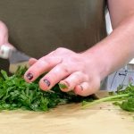 Woman in green shirt chopping cilantro on a manila cutting board