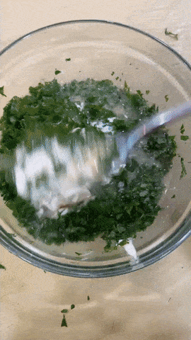 person stirring creamy chimichurri sauce with fork in clear bowl