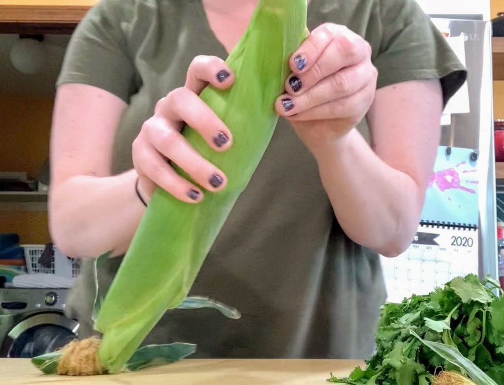 Woman in green shirt shucking an ear of corn