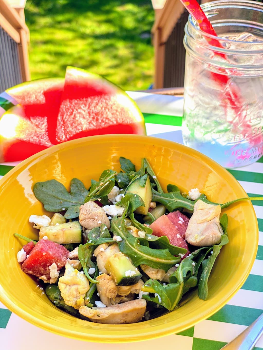 yellow bowl with watermelon salad, ice drink, and slices of watermelon on green and white tray outside