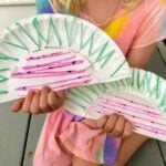 child holding two paper plate watermelon