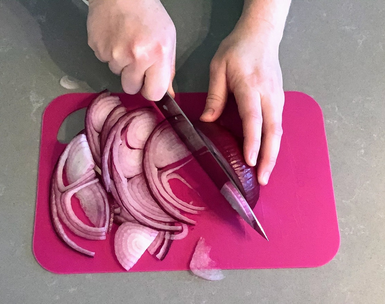 Hands Slicing red onion on pink cutting board for panzanella salad