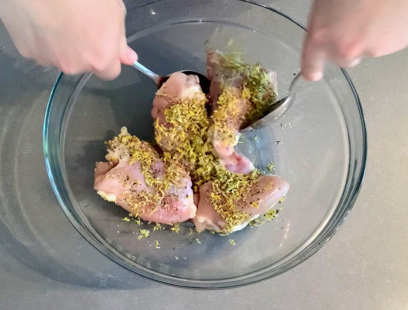 Hands tossing chicken and flavorings, in a clear bowl