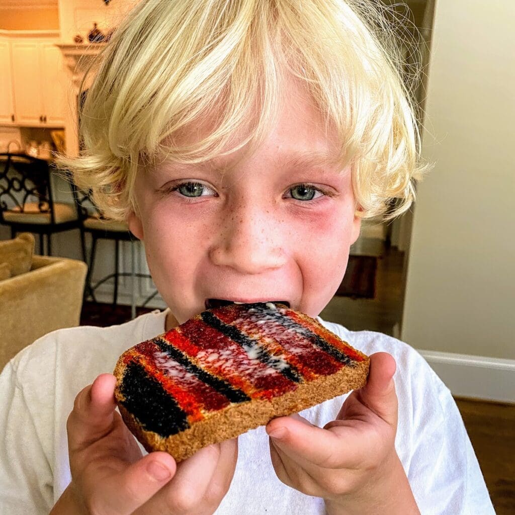 blonde boy eating piece of toast that's painted with striped of different colors