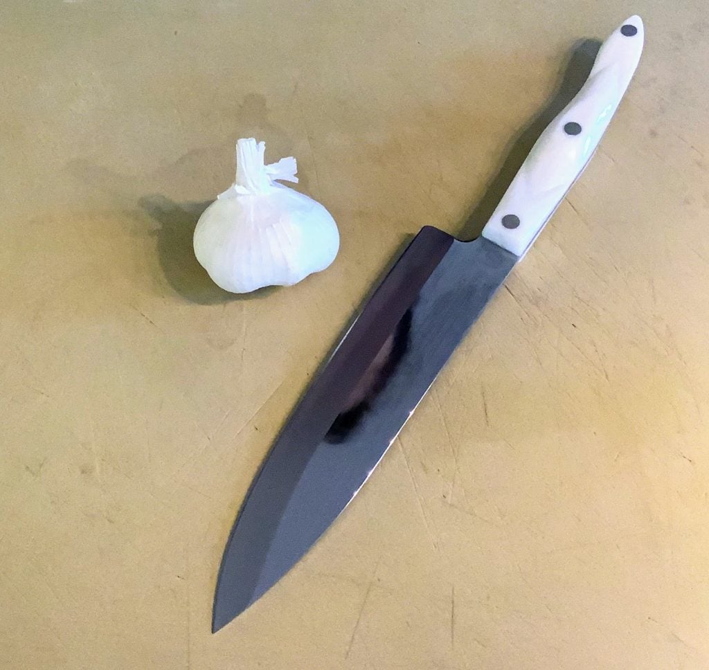 garlic bulb and chef's knife on manila cutting board