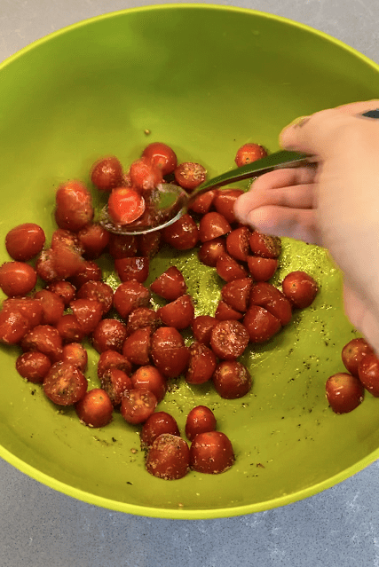 mixing cut baby tomatoes and spices in a large green bowl